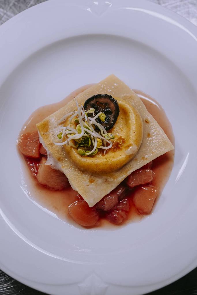 Hausgemachte Ravioli mit schwarzer Walnuss, feiner Garnitur und Holler-Pfirsich-Sud auf einem Teller